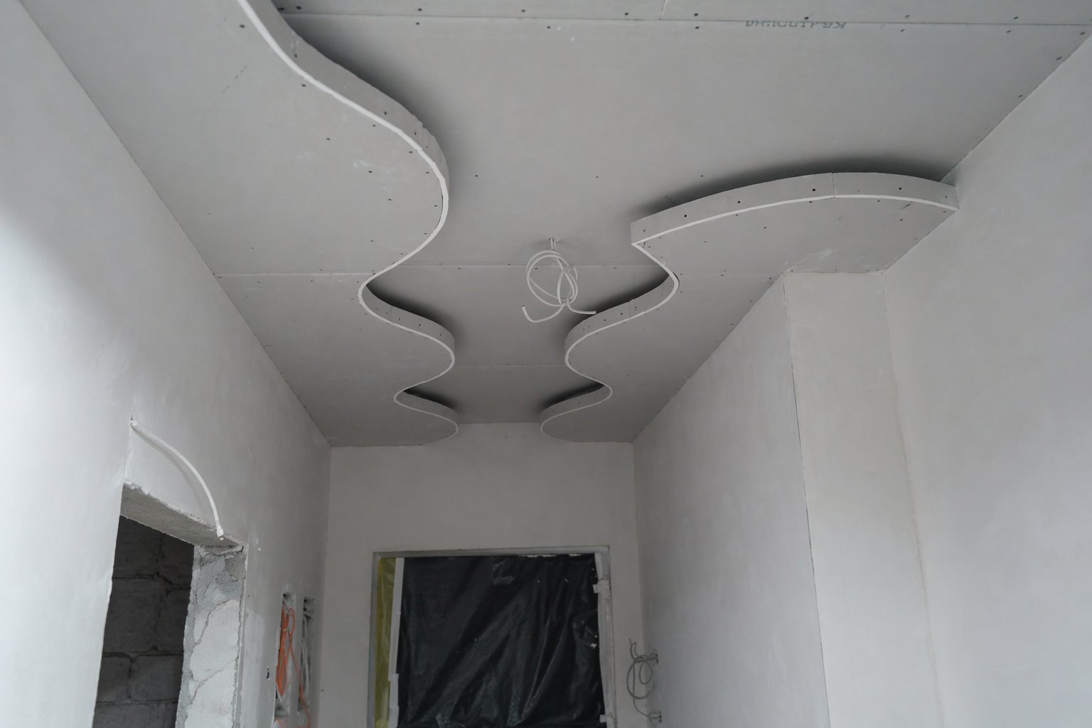 White ceiling with curved ductwork and ventilation system installed in a hallway with white walls