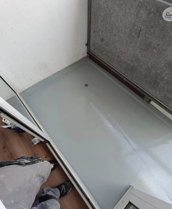 Empty white shower or bathtub base with gray tile wall and wood flooring visible at bottom